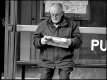 Older man reading tabloid at bus stop P1013016.JPG